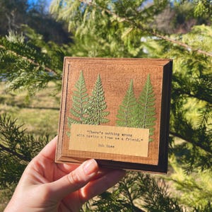 May include: A wooden plaque featuring a pressed fern design and a quote by Bob Ross: "There's nothing wrong with having a tree as a friend."