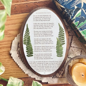 May include: Oval wooden plaque with a poem and pressed ferns. The text is in black, with the title "AN UNEXPECTED PARTY" at the top. The plaque is surrounded by a wooden frame and a white border.