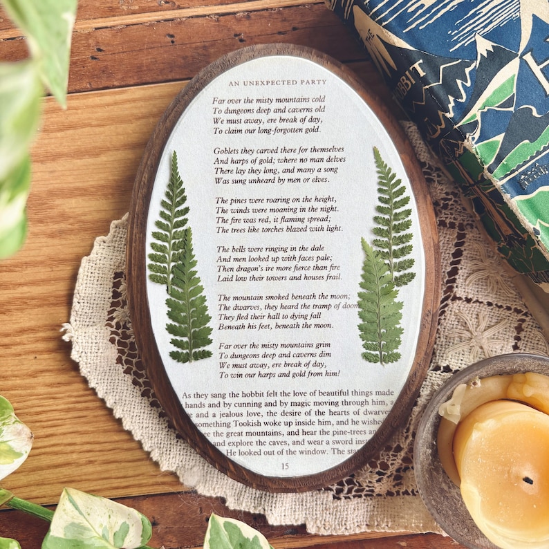 May include: Oval wooden plaque with a poem and pressed ferns. The text is in black, with the title "AN UNEXPECTED PARTY" at the top. The plaque is surrounded by a wooden frame and a white border.
