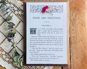 May include: A vintage book cover with a dried rose on top. The title of the book is "Pride and Prejudice" and the chapter is "Chapter I". The text on the cover reads: "It is a truth universally acknowledged, that a single man in possession of a good fortune must be in want of a wife."