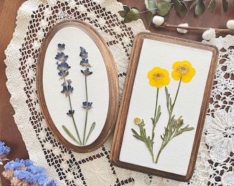 May include: Two framed pressed flower art pieces. The first piece features lavender flowers in shades of purple and blue. The second piece features yellow buttercup flowers.