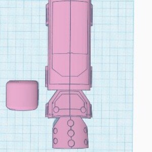 May include: A pink 3D-printed model of a futuristic device, possibly a component of a larger machine or vehicle. The design features a cylindrical body, rectangular base, and a separate cube-shaped piece. The model is set against a grid background.