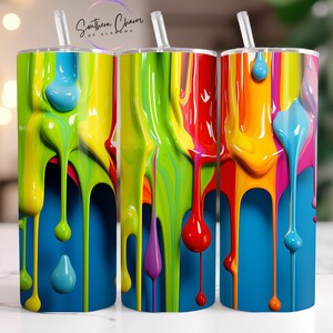 May include: Three colorful paint-splattered tumblers with a blue background. The tumblers are decorated with dripping paint in various colors, including yellow, green, red, purple, and blue.