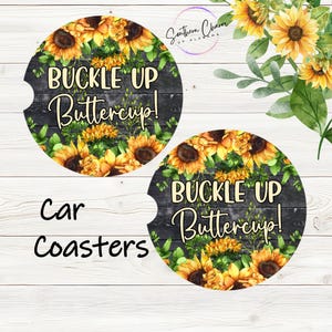 May include: Two round car coasters with a black background and a sunflower design. The text "Buckle Up Buttercup!" is written in white on the coasters.