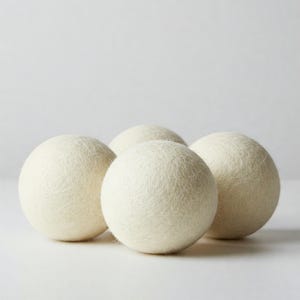 May include: Four white wool dryer balls. The balls are soft and fluffy and are used to help reduce drying time and soften clothes.