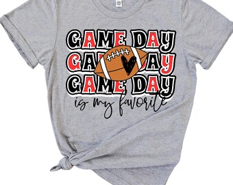 Op de afbeelding: Grijs T-shirt met de tekst "GAME DAY is my favorite" in zwart en rood. Een voetbal met een hartje bevindt zich in het midden van de tekst.