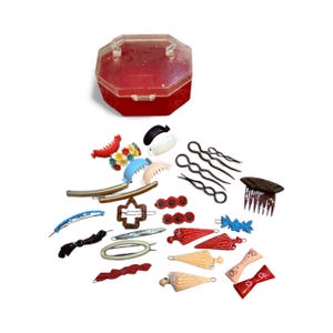 May include: A collection of vintage hair accessories, including barrettes, bobby pins, and combs, in various colors and designs. A red, octagonal plastic case is at the top. The accessories are scattered on a white surface.