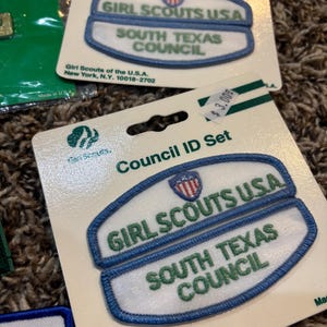 May include: Council ID Set patches for Girl Scouts. The patches are white with blue trim and feature the text "GIRL SCOUTS USA" and "SOUTH TEXAS COUNCIL" in green. The patches are on a cardboard backing.