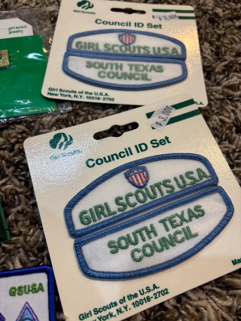 May include: Council ID Set patches for Girl Scouts. The patches are white with blue trim and feature the text "GIRL SCOUTS USA" and "SOUTH TEXAS COUNCIL" in green. The patches are on a cardboard backing.