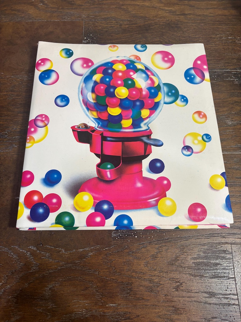 Puede incluir: Un cuaderno blanco con una ilustraci&oacute;n vibrante de una m&aacute;quina de chicles. La m&aacute;quina es de color rosa brillante con un globo transparente lleno de chicles de colores. Hay chicles flotantes de varios colores esparcidos.