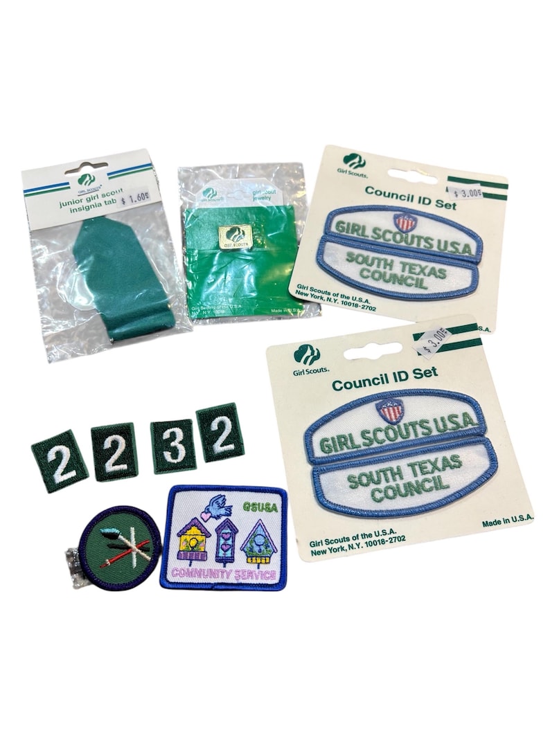 May include: A collection of Girl Scout patches and insignia tabs. Includes a green insignia tab, Council ID sets with blue and white patches, number patches, and a Community Service patch with birdhouses.