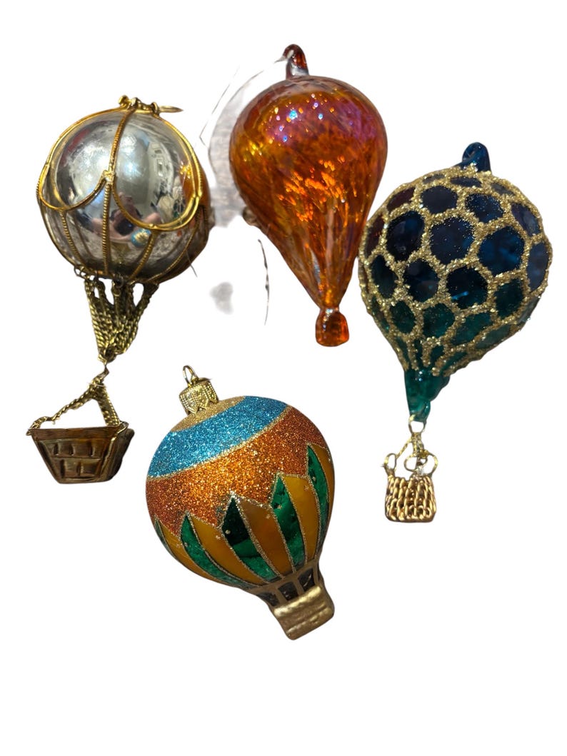 Może przedstawiać: Kolekcja ozd&oacute;b w kształcie balon&oacute;w na ogrzane powietrze. Ozdoby mają r&oacute;żne wzory, w tym srebrny balon z lustrem ze złotą klatką, błyszczący pomarańczowy kształt łzy oraz niebiesko-złoty wz&oacute;r plastra miodu. Czwarta ozdoba ma niebieski, pomarańczowy i zielony wz&oacute;r.