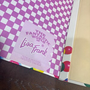 Puede incluir: Libro abierto con un patr&oacute;n de cuadros morados y blancos en la cubierta interior. Es visible una pegatina con el texto "The Fantastic World of Lisa Frank". El borde del libro tiene formas geom&eacute;tricas coloridas.
