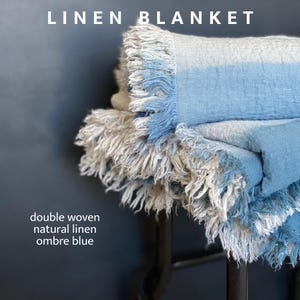 May include: A double woven linen blanket in shades of blue and natural. The blanket has a fringed edge and the text "LINEN BLANKET" at the top. The text "double woven natural linen ombre blue" is at the bottom.
