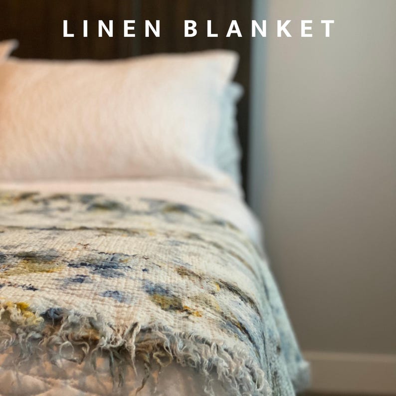 May include: A bed with a white pillow and a patterned linen blanket. The blanket has a frayed edge and a design with blue, yellow, and brown hues. The text "LINEN BLANKET" is at the top of the image.