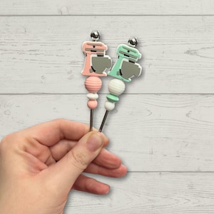 Peut inclure: Deux bâtonnets à sucettes avec un thème de batteur sur socle. Un bâtonnet est rose avec des perles blanches et l'autre est vert avec des perles blanches.