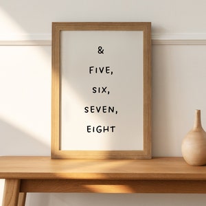Puede incluir: Una impresión enmarcada con el texto "& FIVE, SIX, SEVEN, EIGHT" en un estante de madera clara con un jarrón de madera y una bola de madera.
