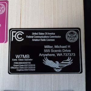 May include: Black and gold amateur radio license cards with the Federal Communications Commission logo and the text "United States of America" and "Amateur Radio Licensee". The top card has the call sign "W7MB" and the name "Miller, Michael H" with an address and grant date. The bottom card has the call sign "FC".