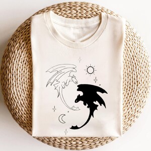 May include: White t-shirt with a black and white illustration of two dragons, one white and one black, with stars, a sun, and a moon in the background.