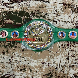 May include: A green and gold boxing championship belt with the WBO logo and multiple flags. The belt has a centre plate with the words "World Boxing Organisation" and "WBO" in gold lettering.