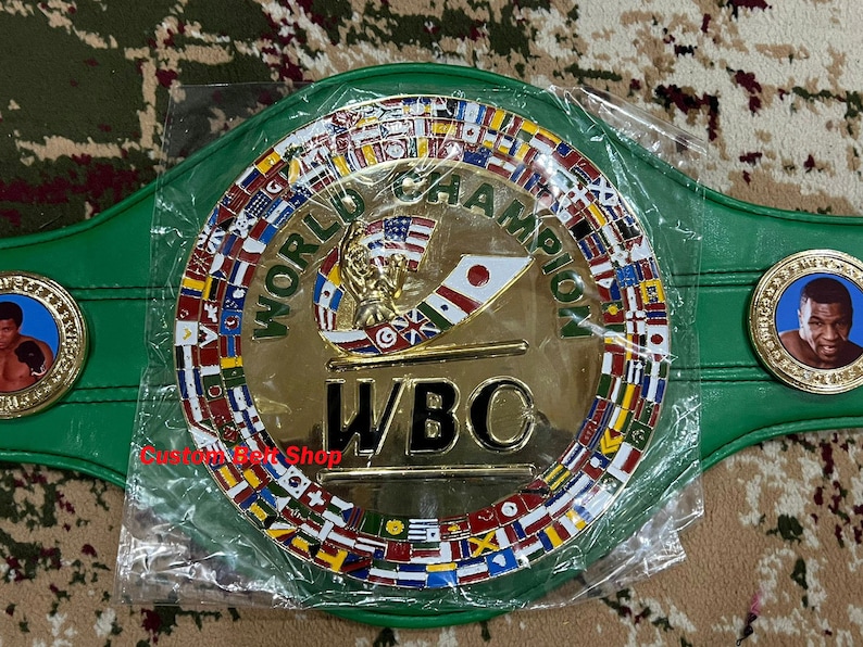 May include: A green and gold World Boxing Council (WBC) championship belt with a gold plate featuring the WBC logo and the words "World Champion". The belt is decorated with a circle of flags representing different countries.