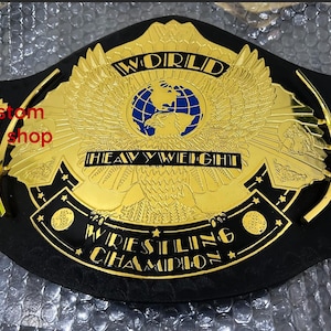May include: A gold wrestling championship belt with a black leather strap. The belt features a large central plate with an eagle, globe, and the words "WORLD HEAVYWEIGHT WRESTLING CHAMPION".