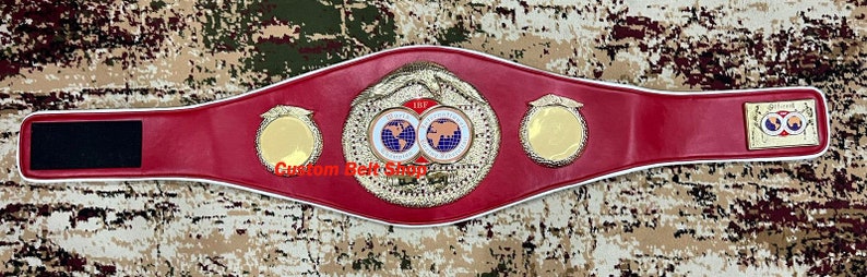 Op de afbeelding: Een rode leren bokskampioensgordel met gouden accenten en een witte rand. De riem heeft twee ronde platen met een wereldbeeld en de tekst "World Boxing Union" en "Custom Belt Shop".