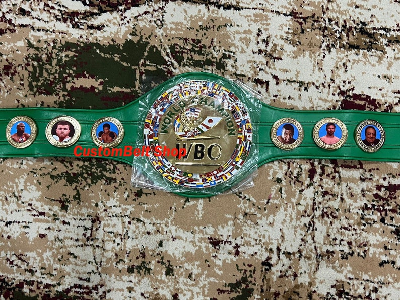 Op de afbeelding: Een groene en gouden bokskampioensgordel met het WBO-logo en meerdere vlaggen. De gordel heeft een middelste plaat met de woorden "World Boxing Organization" en "WBO" in gouden letters.