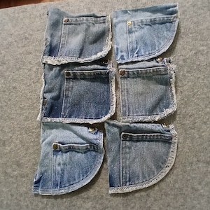 May include: Seven light blue denim pockets with metal button closures and frayed edges are arranged on a gray surface. The pockets are cut from jeans and have a curved bottom edge. The pockets are arranged in a grid pattern.