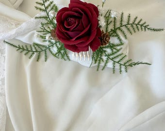 Puede incluir: Un peine para el cabello con una rosa burdeos, helechos verdes y acentos de flores blancas. El arreglo floral incluye una pequeña piña y está colocado en un peine blanco. Perfecto para bodas u ocasiones especiales.