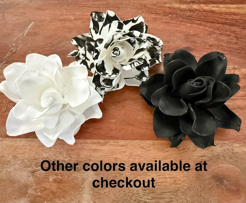 Puede incluir: Tres decoraciones de flores artificiales en blanco, negro y blanco y negro. La flor blanca tiene m&uacute;ltiples capas de p&eacute;talos. La flor en blanco y negro tiene un patr&oacute;n moteado. La flor negra tiene un dise&ntilde;o de p&eacute;talos en capas. El texto en la parte inferior dice "Otros colores disponibles al finalizar la compra."