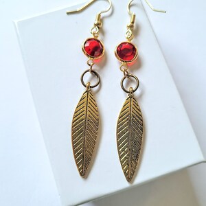 May include: Gold dangle earrings with red gemstone accents and a leaf design.
