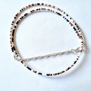 May include: A layered necklace with black, white, and copper beads. The necklace has a silver chain clasp.
