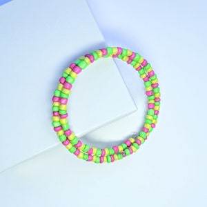 May include: A green and pink beaded bracelet with a silver clasp. The bracelet is wrapped around itself twice.
