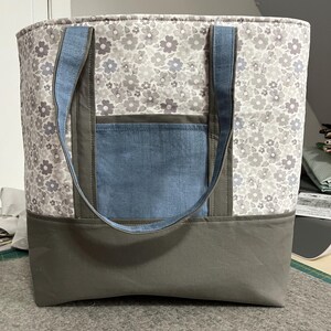 May include: A large gray and white floral tote bag with a blue denim pocket and gray handles.