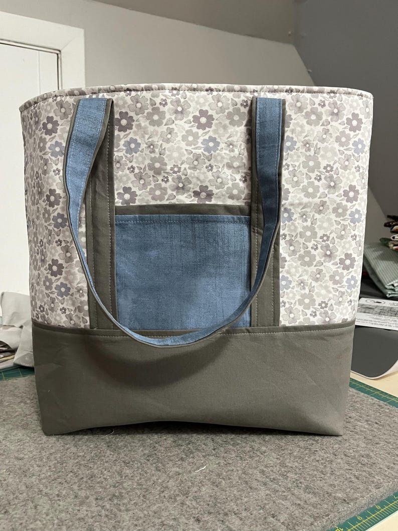 May include: A large gray and white floral tote bag with a blue denim pocket and gray handles.