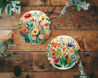 Könnte beinhalten: Zwei runde Auto-Untersetzer mit floralem Design. Die Untersetzer zeigen eine Vielzahl farbenfroher Blumen, darunter rote, rosa, gelbe und blaue Blüten, vor einem cremefarbenen Hintergrund. Die Untersetzer werden auf einer Holzoberfläche präsentiert.