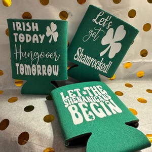 Può includere: Tre refrigeratori per lattine in schiuma verde con testo bianco e disegni di trifoglio. I refrigeratori dicono "Irish Today Hangover Tomorrow", "Let's Get Shamrocked!" e "Let the Shenanigans Begin".