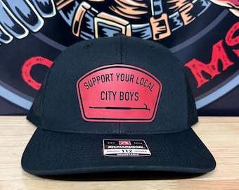 May include: Black trucker hat with a red patch that reads "SUPPORT YOUR LOCAL CITY BOYS" in white text. The hat has a curved brim and an adjustable strap. The brand is Richardson 112.