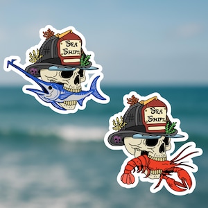 May include: Two stickers featuring a skull wearing a firefighter helmet with the text "Sea Shift". One skull has a blue marlin in its mouth, the other has a red lobster. The background is a blurred ocean.