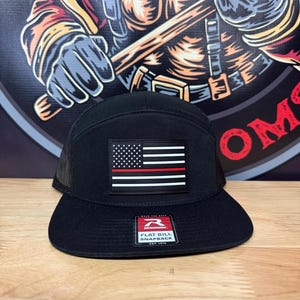 May include: Black flat bill snapback hat with a mesh back and a US flag patch with a red stripe. The hat has a flat peak and a snapback closure. The Richardson brand tag is visible.