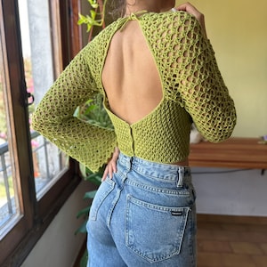 May include: A lime green crochet top with a large open back and long sleeves. The top is cropped and has a loose fit.