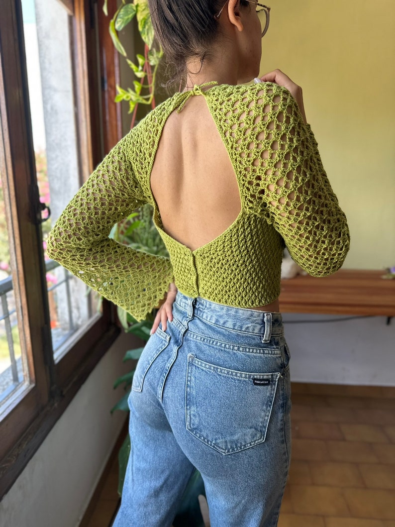 May include: A lime green crochet top with a large open back and long sleeves. The top is cropped and has a loose fit.