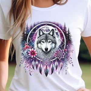 Pode incluir: Camiseta branca com um design de apanhador de sonhos colorido que apresenta uma cabeça de lobo, flores e penas. O apanhador de sonhos é rodeado por um fundo de galáxia roxo e azul.
