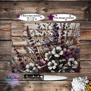 May include: A rectangular cutting board with a floral design featuring white, purple, and pink flowers against a wood-grain background. The board measures 16" x 12" and 11" x 8". A knife is placed below the board.
