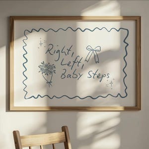 Könnte beinhalten: Ein gerahmter Druck mit einem hellen Holzrahmen. Der weiße Hintergrund zeigt einen blauen Wellenrand und blaue Illustrationen eines Blumenstraußes, einer Schleife und Sterne. Der Text lautet "Right, Left, Baby Steps."