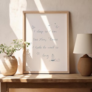 Könnte beinhalten: Ein gerahmter Druck mit dem Text "I sleep so I can See You, 'Cause I hate to wait so long" in blauer Schrift. Der Druck befindet sich in einem hellen Holzrahmen und wird auf einem Holztisch ausgestellt. Eine Lampe und eine Vase mit einer Pflanze stehen ebenfalls auf dem Tisch.