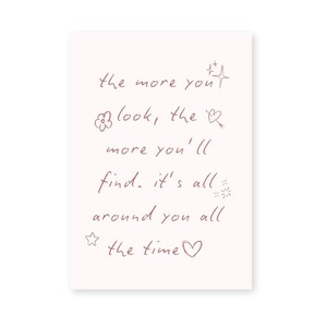 May include: A rectangular, off-white card with handwritten text in a soft, reddish-brown color. The text reads: "the more you look, the more you'll find. it's all around you all the time."
