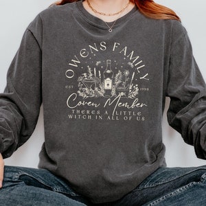 Könnte beinhalten: Ein schwarzes Langarmshirt mit einem weißen Grafikdruck, auf dem "Owens Family Est. 1998 Coven Member There's a little witch in all of us" steht.