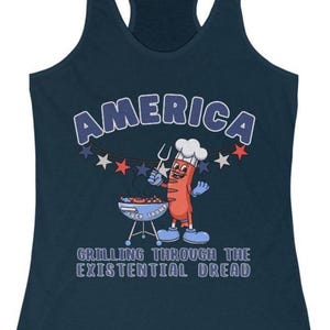 May include: Navy blue tank top with the word "AMERICA" in white outlined in blue. A cartoon hot dog character is grilling on a barbecue. The text "GRILLING THROUGH THE EXISTENTIAL DREAD" is below the graphic.